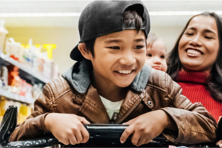 Un padre de familia sonriente empujando a su hijo en un carrito de compras en un supermercado
