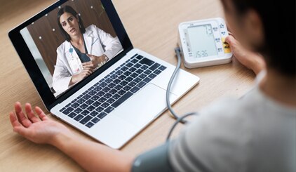 Paciente usando un dispositivo de monitoreo en el hogar mientras habla con el médico desde una computadora portátil