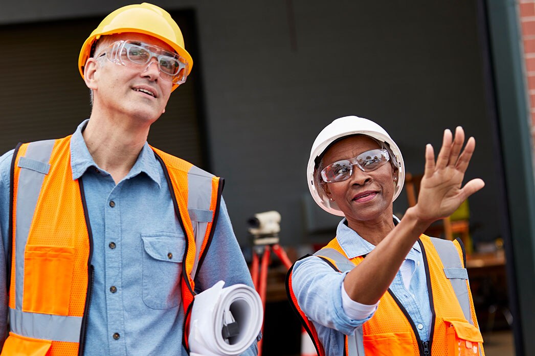 Workers carrying building plans discuss construction