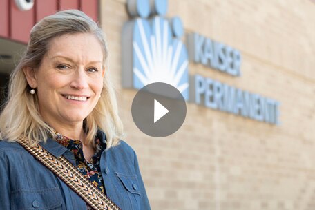 : Video play button over image of Kaiser Permanente Colorado member standing in front of medical office building
