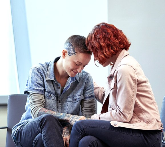 Dos personas transgénero tocándose cabeza con cabeza en una oficina