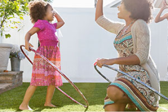 Una mujer y sus hijos jugando con aros de hula-hula y un balón en el jardín