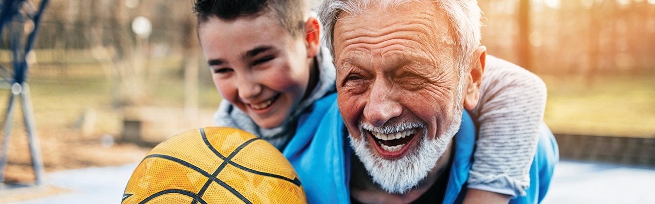 Persona mayor sonriente con su nieto en una cancha de básquetbol