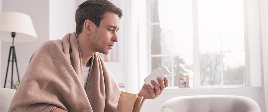 Persona envuelta en una cobija mirando un frasco de pastillas