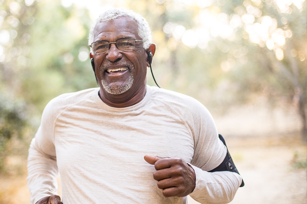Una persona mayor sonríe mientras corre con auriculares puestos