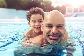 Niño abrazado a los hombros de su padre en una piscina  
