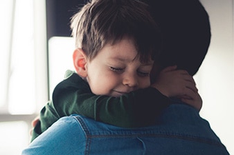 Niño llorando y abrazando a un adulto después de una pesadilla.