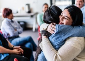 Dos personas se abrazan durante una reunió de un grupo comunitario.
