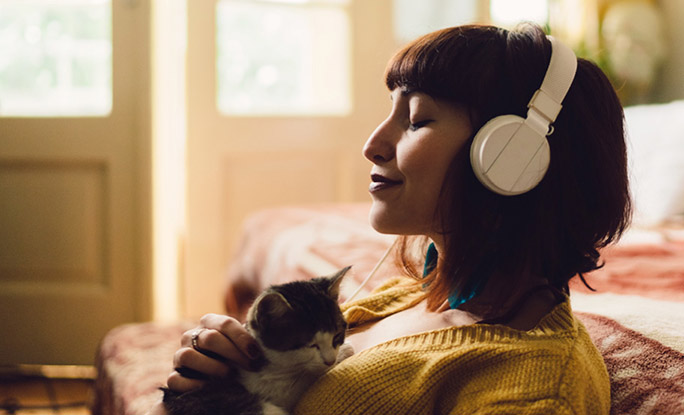 Persona feliz sosteniendo un gatito y escuchando con auriculares