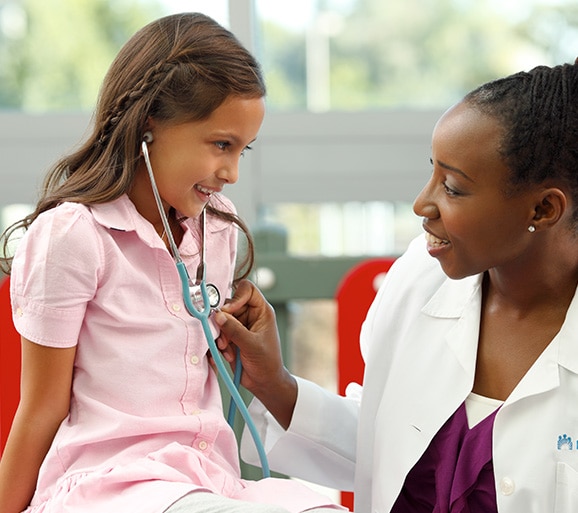 Médica revisando los latidos del corazón de una niña sonriente
