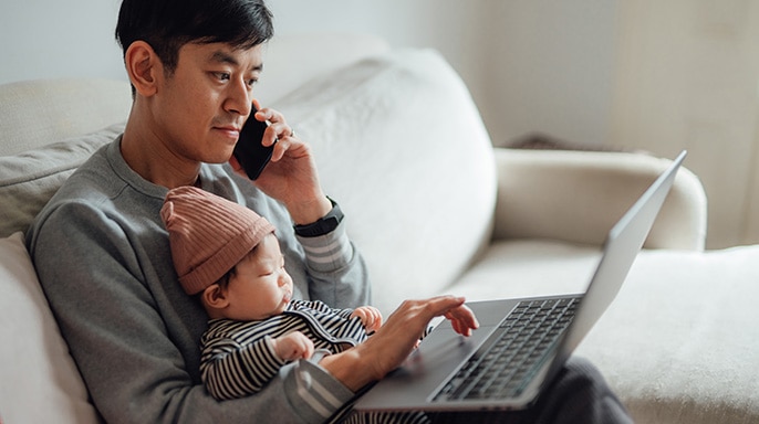 Padre hablando por teléfono y trabajando en la computadora con su bebé en el regazo