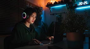 Adolescente con auriculares sentado en una computadora bajo una luz azul