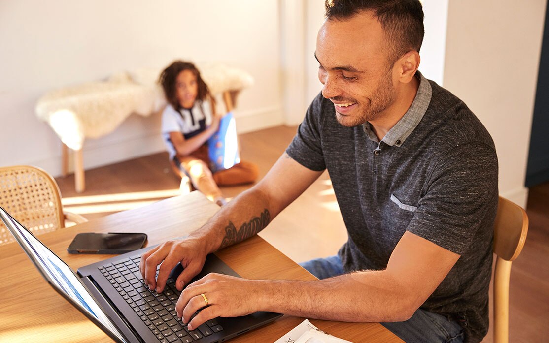 man typing on computer with son in background