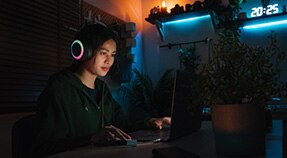 Adolescente con auriculares sentado en una computadora bajo una luz azul